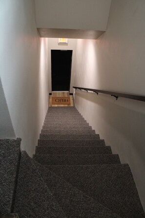 A staircase with carpeted steps, a handrail, and a wooden door at the top with a 'HELLO' sign.
