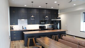 A modern kitchen with dark cabinetry, a wooden island, bar stools, and a seating area with a bench and cushions.
