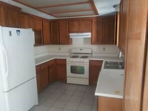 A kitchen with wooden cabinets, a white refrigerator, a stove, and a sink. - Lovely 1-bedroom house with AC in charming Twentynine Palms (Twentynine Palms)