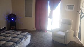 Een slaapkamer met een bed, een stoel, een raam met gordijnen en een airconditioning.