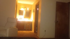 Een kamer met een bed, een stoel, een kaptafel met spiegel en een deur.