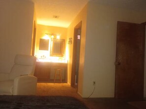 A room with a bed, a chair, a vanity with a mirror, and a door. - Lovely 1-bedroom house with AC in charming Twentynine Palms (Twentynine Palms)