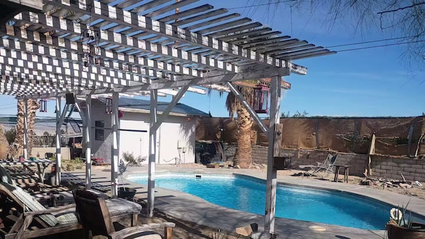 Een achtertuin met een zwembad, een pergola en tuinmeubilair.