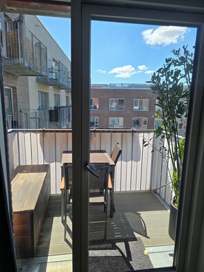 Un balcon avec une table et des chaises en bois, un banc et un pot de fleurs.
