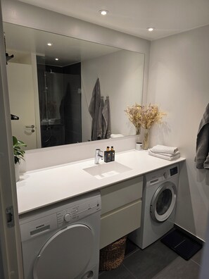 Une salle de bain moderne avec un grand miroir, un lavabo, un lave-linge et un porte-serviettes.