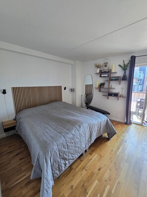 Une chambre moderne avec un grand lit, une tête de lit en bois, des tables de chevet, un miroir et une étagère intégrée agrémentée d’objets décoratifs.