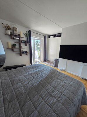Quarto moderno com uma cama grande, estantes embutidas, uma TV e uma porta de correr de vidro para o exterior.