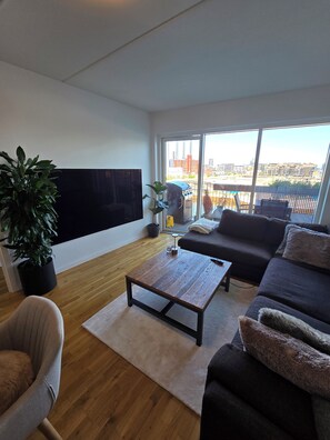 Uma sala de estar moderna com uma TV de tela plana, um sofá, uma mesa de centro e um vaso com planta.