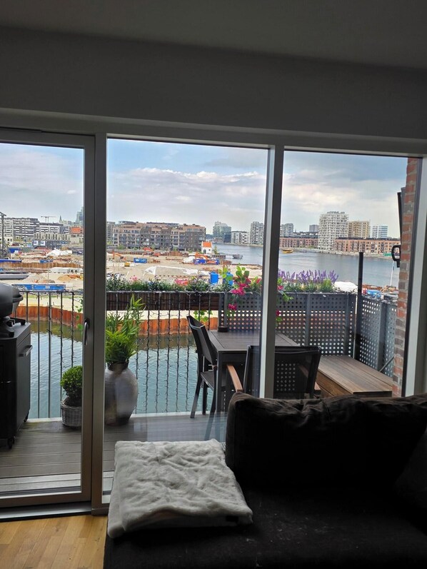 Un balcon donnant sur une rivière et des immeubles, un canapé, une table et des chaises.
