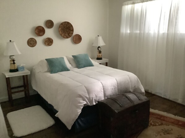 A bedroom with a bed, two bedside tables, a nightstand, a dresser, and a window with curtains. - Soothing 1-bedroom cottage with AC in charming Clyde.  Located on quiet 5 acres (Clyde)