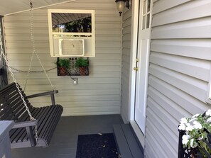 A porch with a bench, a small window with air conditioning, and a door.