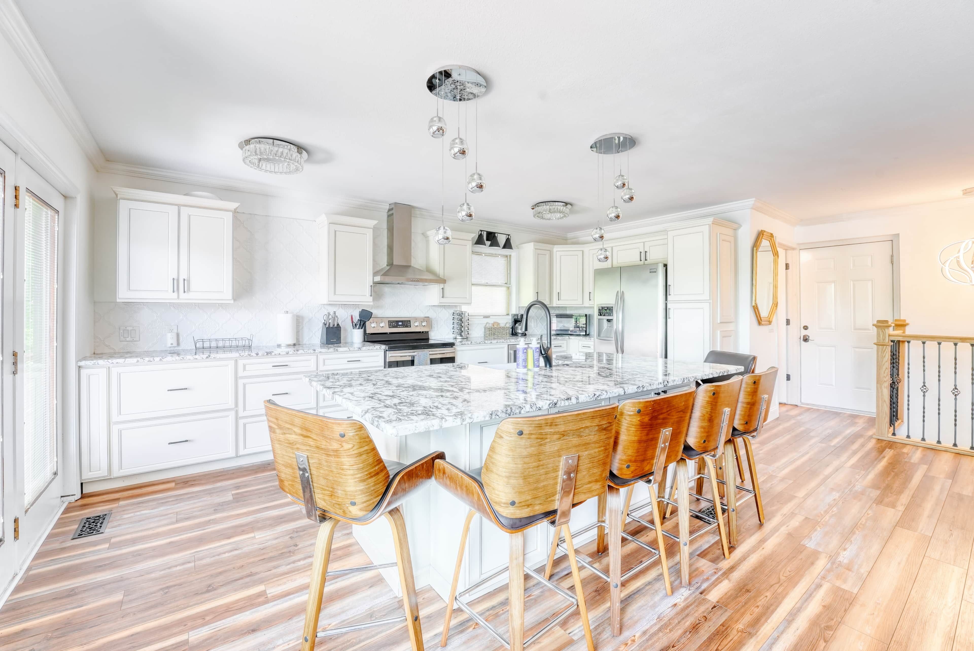 Una cocina moderna con gabinetes blancos, una isla de mármol y taburetes de madera.