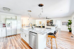 Una cocina moderna con armarios blancos, un refrigerador de acero inoxidable, una isla de mármol y un ventilador de techo.
