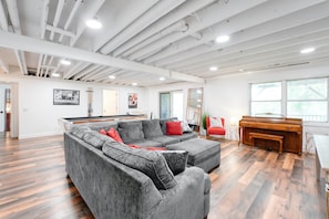Una habitación amplia con un sofá seccional gris, un piano de madera y una mesa de billar.