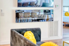 A modern living room with a sofa, a flat-screen TV mounted on the wall, and a dining area with chairs and a table. - Dockside Retreat on the Lake- Private Dock- Kayaks- Close to Bike Trails (Bella Vista)