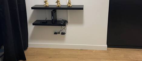 Een woonkamer met een flatscreen televisie aan de muur, een zwart entertainment meubel eronder en een ronde salontafel met decoratieve objecten.