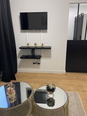 Un salon doté d’un téléviseur à écran plat fixé au mur, d’un meuble de rangement noir en dessous et d’une table basse ronde agrémentée d’objets décoratifs.