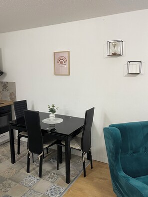 Et spiseområde med et sort bord og stole, en turkis sofa og en lille plante på bordet.