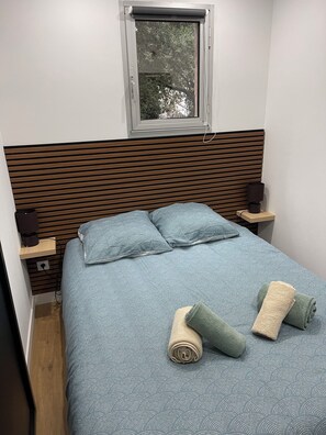 Ein Schlafzimmer mit Bett, Kissen, Fenster, Nachttisch und Lampe.