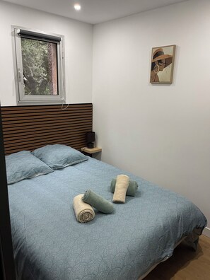 Et soveværelse med en seng, puder, et natbord, en lampe, et vindue og et billede på væggen.