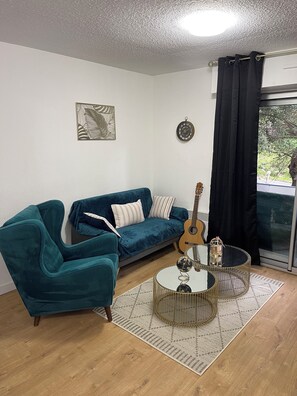 Un salon avec un canapé de couleur turquoise, un fauteuil bleu, une guitare et une table basse ronde.