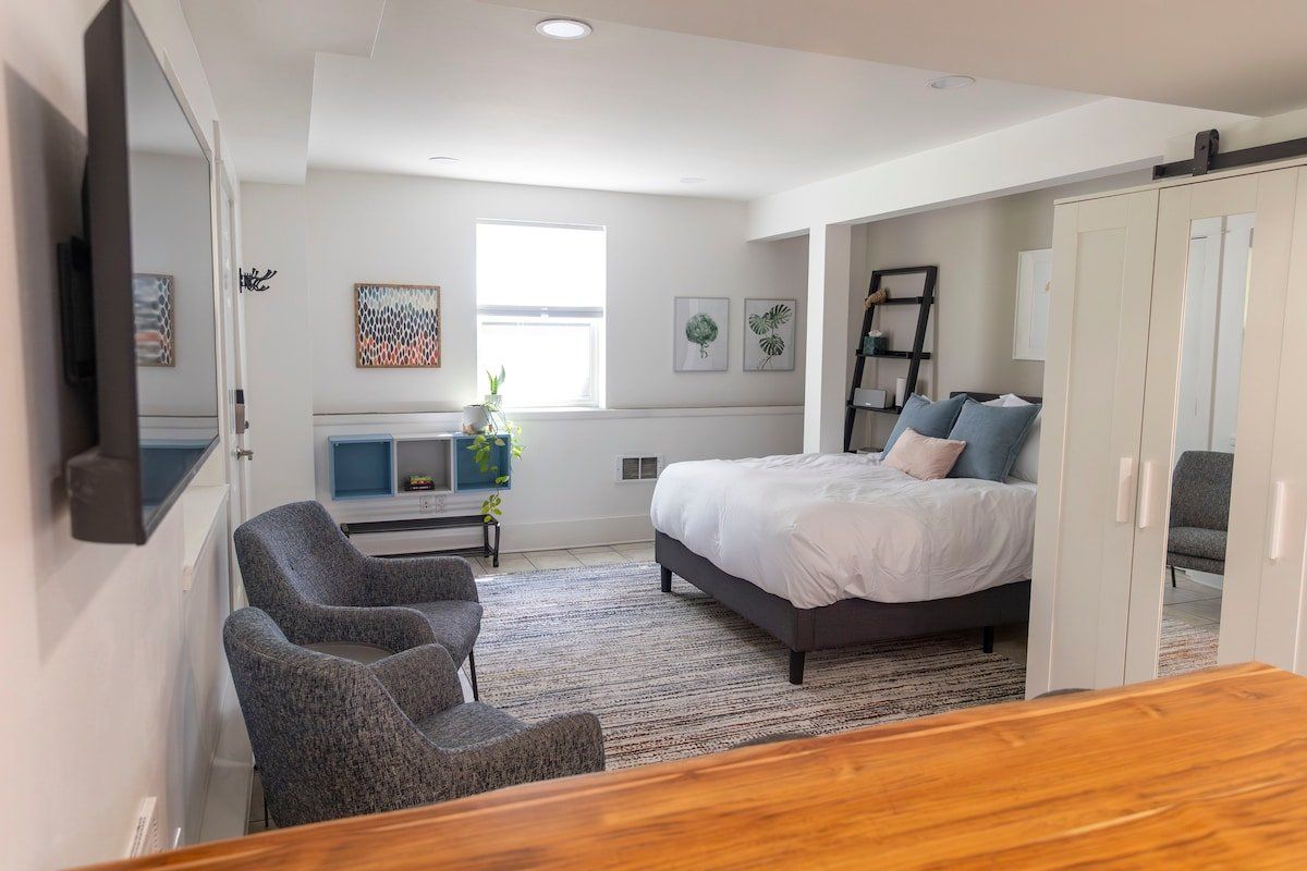 A bedroom with a bed, two chairs, a desk, and a wardrobe.