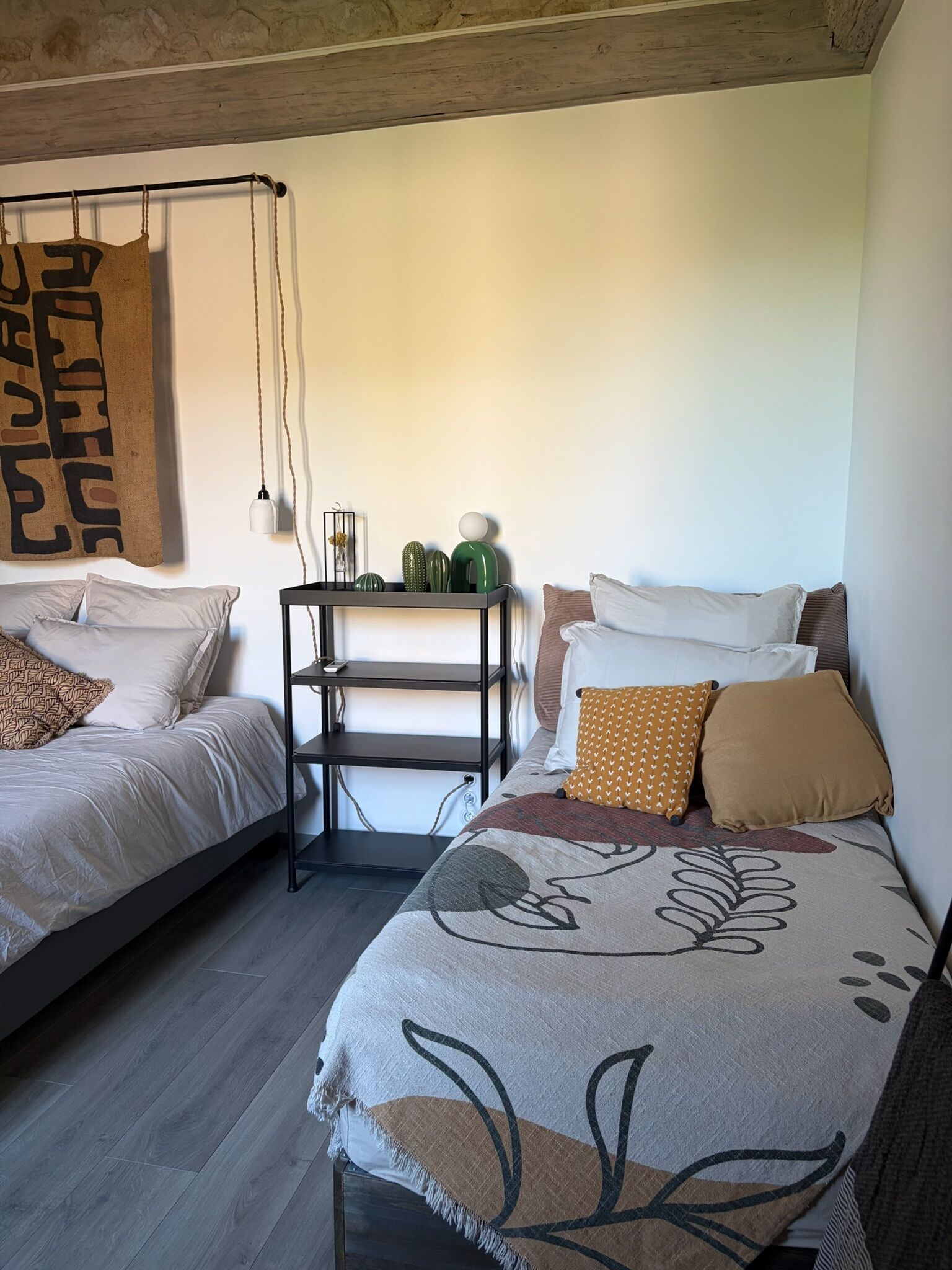Een slaapkamer met twee bedden, een nachtkastje met decoratieve objecten en een hangend wandtapijt.