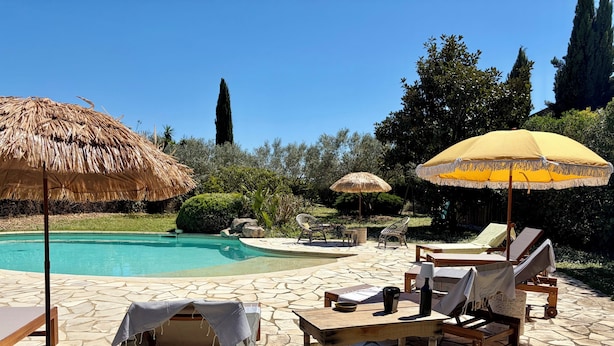 Area piscina con sedie a sdraio, un tavolo e un ombrellone di paglia.