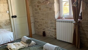 Una stanza con parete in pietra, un letto con asciugamani arrotolati, un termosifone e una finestra con tende.