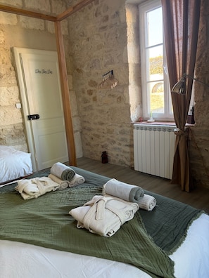 A room with a stone wall, a bed with rolled towels, a radiator, and a window with curtains.