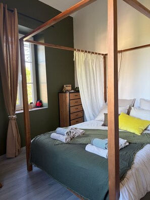 Una cama con dosel, con una colcha verde, almohadas blancas y una almohada amarilla.