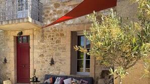 Un edificio in pietra con una porta rossa, un balcone con ringhiere in metallo, un divano con cuscini e un vaso con una pianta.