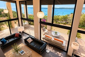 Ein modernes Interieur mit großen Fenstern, einer schwarzen Ledersofa, einem weißen Sofa und einem Essbereich mit Tisch und Stühlen.