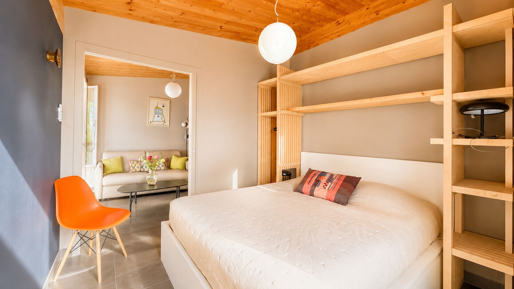 A bedroom with a bed, a chair, a sofa, and a wooden shelf unit.