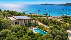 Eine Villa mit Pool, umgeben von üppiger Vegetation und Blick auf das Meer mit Booten.
