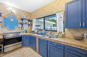 Una cocina con gabinetes azules, una estufa, un lavamanos y un ventanal con vistas.