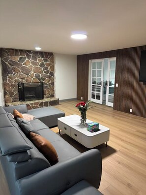 Ein modernes Wohnzimmer mit Steinwand, grauem Sofa, weißem Couchtisch und Kamin.