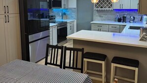 Een moderne keuken met een centraal eiland, hanglampen en een eetgedeelte met een geruit tafelkleed.