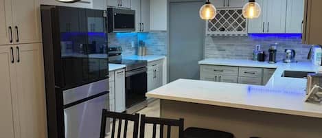 A modern kitchen with a central island, pendant lights, and a dining area with a checkered tablecloth.
