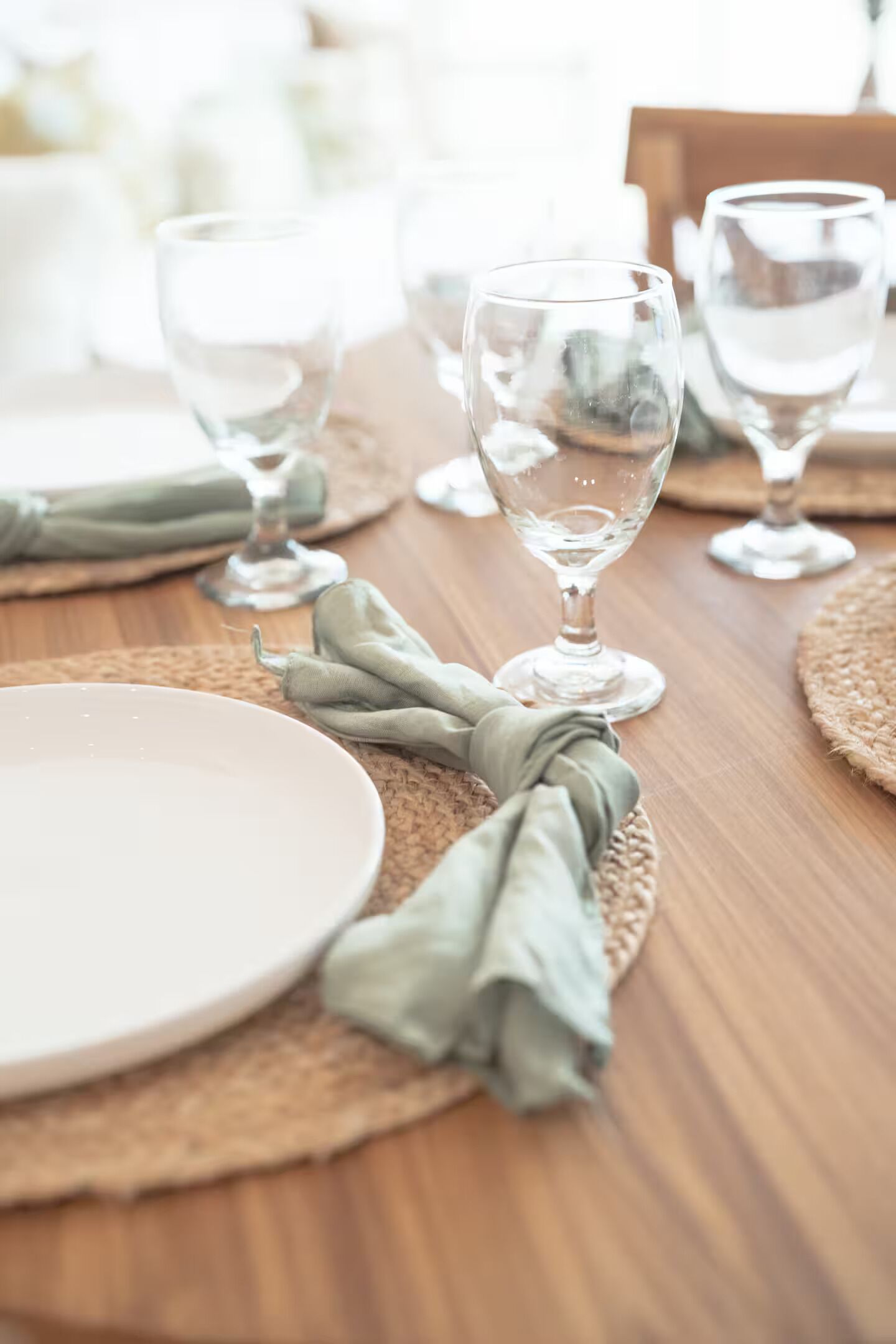 A dining table with clear glassware, a white plate, and a green cloth napkin.