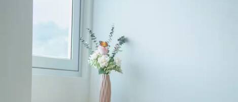 Un bureau d’angle agrémenté d’un vase de fleurs, une fenêtre et un mur blanc.