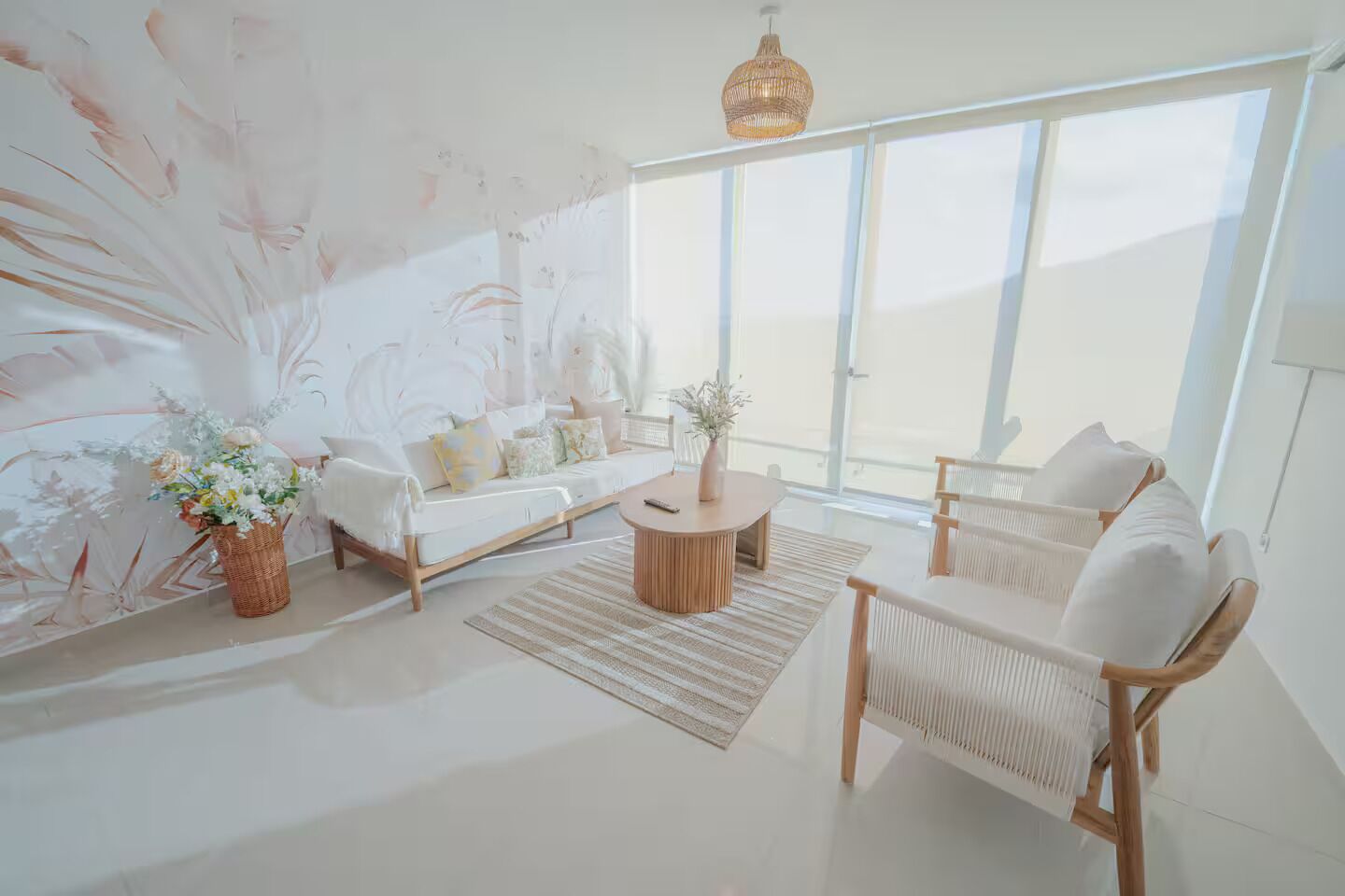 Una sala de estar moderna con sofá, mesa de centro y sillones, ventanas amplias y un detalle decorativo en la pared.