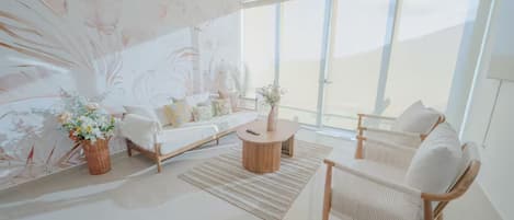 Una sala de estar moderna con sofá, mesa de centro y sillones, ventanas amplias y un detalle decorativo en la pared.