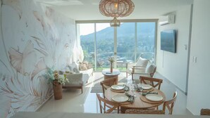 Uma área de refeições com uma mesa posta para quatro pessoas, um sofá e uma janela grande com vista.
