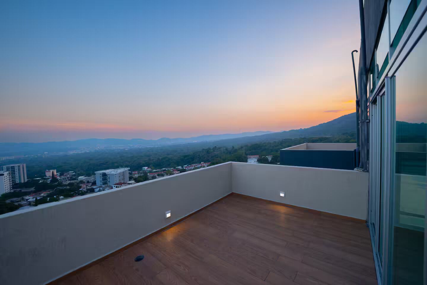 Un balcon offrant une vue sur le paysage urbain et les montagnes au coucher du soleil.