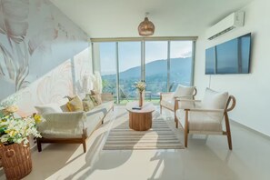 Ein modernes Wohnzimmer mit einer Couch, Sesseln, einem Couchtisch und einem großen Fenster mit Blick auf einen Berg.