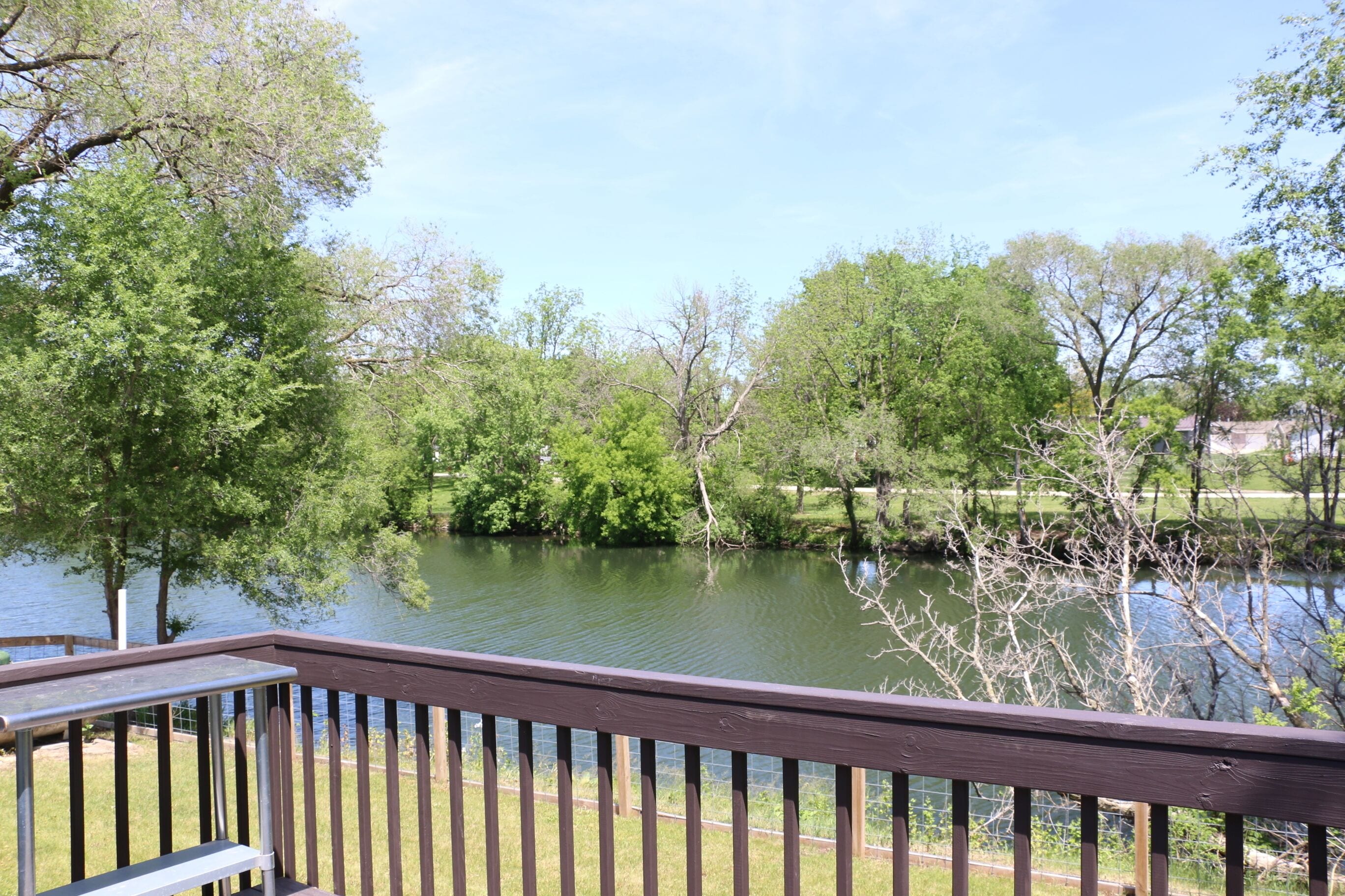 A deck with a view of a calm lake surrounded by trees.. Charming 4 Bedroom Home in Waucoma, Iowa-River front property