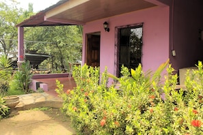 A pink building with a covered porch, a stone pathway, and lush greenery.