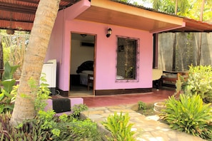 A pink building with a covered porch, a window with decorative ironwork, and a door leading inside.