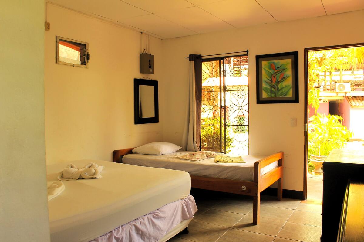A room with two beds, a window with curtains, a framed picture, and a small table.